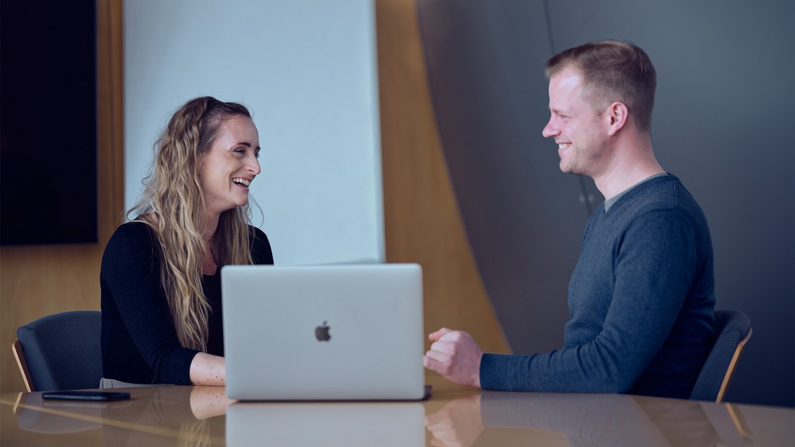 [Translate to China:] A woman and a man talking while sitting in front of a laptop