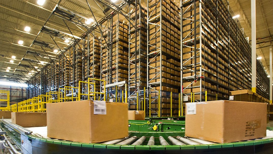 Conveyor belt with carboard boxes travelling on them in front of the metal rackings