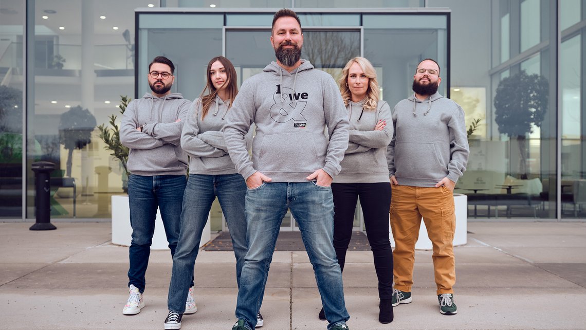 A team picture with the gray brand relaunch hoodies in frond of the building